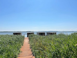 A wooden pathway leading to three modern, elevated structures by a calm lake. - Luxury Houseboat for 2 People, by the sea (gmina Sianów)