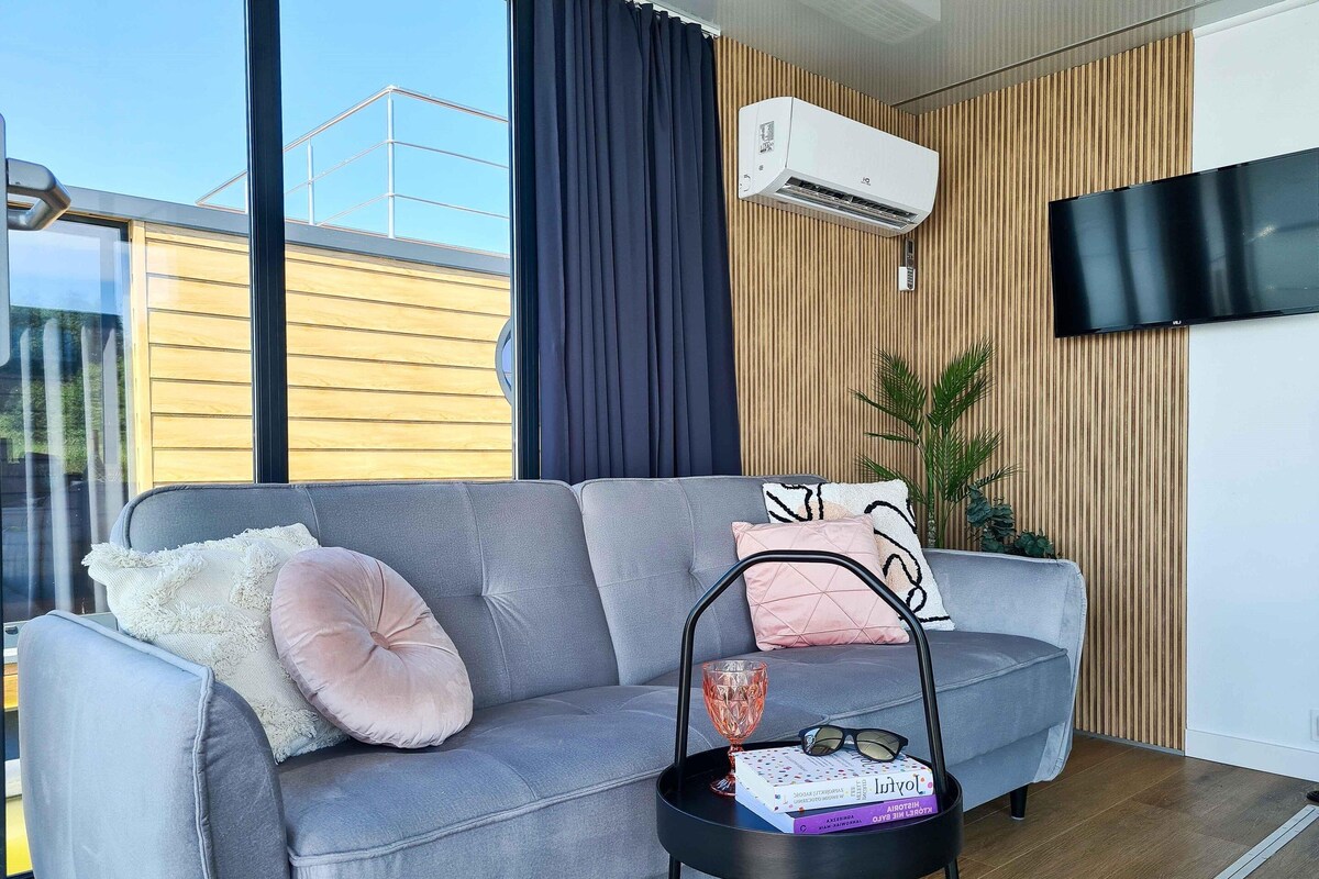 A modern living room with a grey sofa, a small black side table, and a mounted air conditioner.