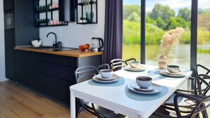 Een moderne keuken met een centraal eiland, een eettafel met stoelen en uitzicht op een meer door grote ramen.