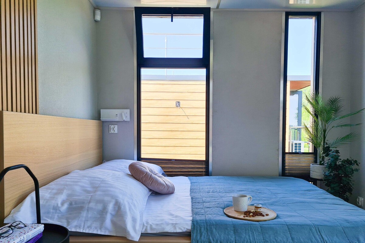 Een moderne slaapkamer met een bed, nachtkastje en een raam met uitzicht.