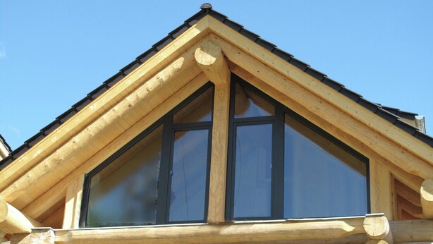 Une cabane en rondins de bois, avec un toit triangulaire et de grandes fenêtres.