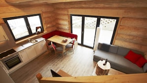 L’intérieur d’une cabane comprend une cuisine, un coin repas et un espace de vie, avec des murs en bois et de grandes fenêtres.