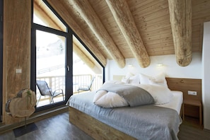 A bedroom with a wooden ceiling, a large bed, a nightstand, and a view of the outdoors.