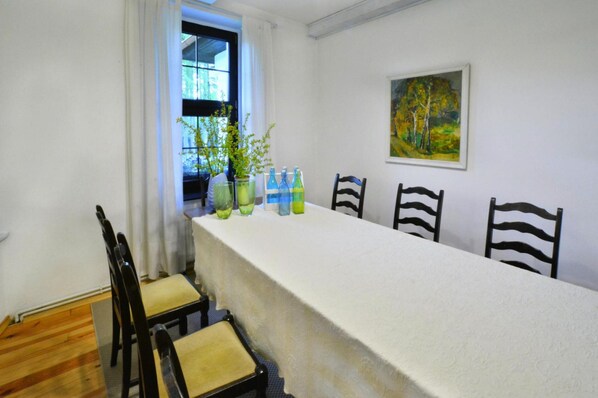 A dining area with a long table, chairs, potted plants, and a painting on the wall.