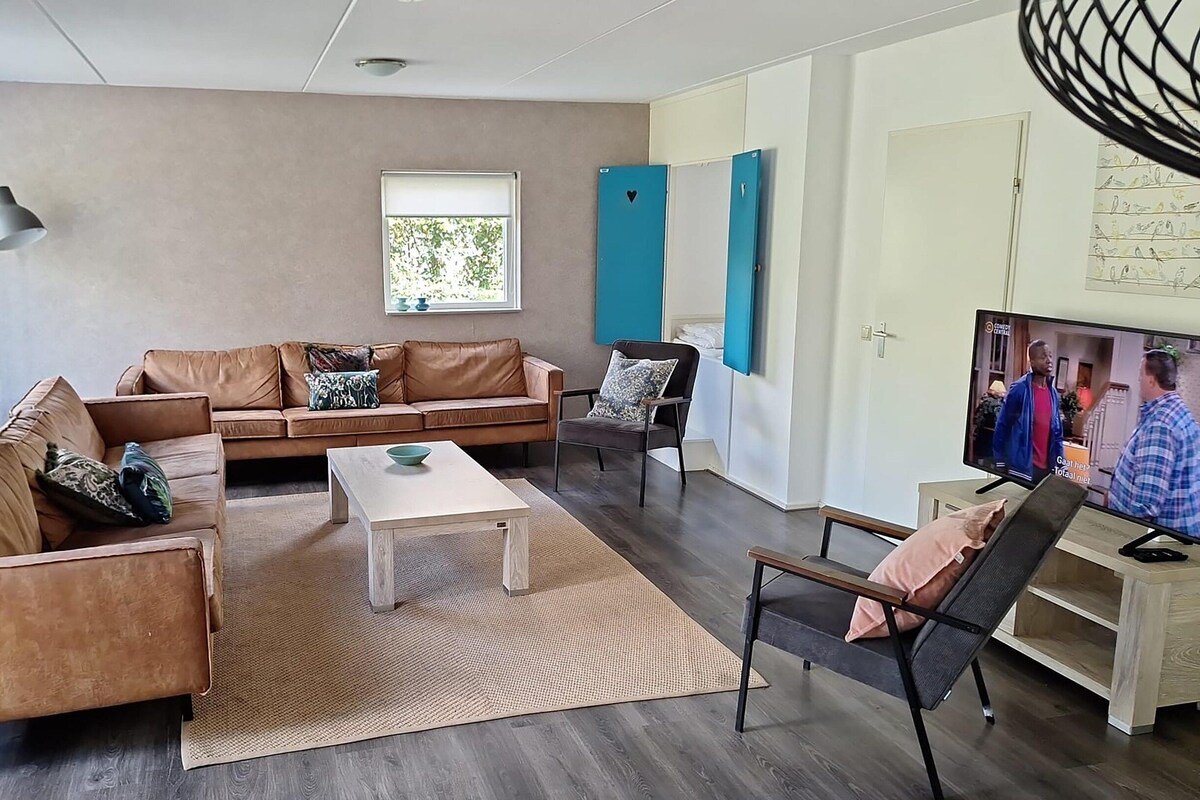 Uma sala de estar moderna com um sofá de couro marrom, uma mesa de centro de madeira e uma TV sobre um suporte.