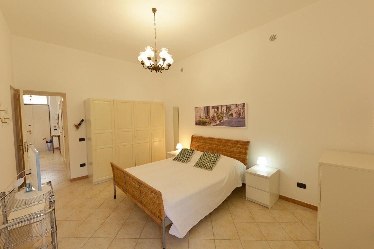 A bedroom with a bed, bedside tables, a wardrobe, a chandelier, and a painting on the wall.