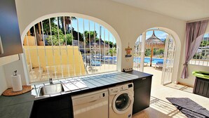 A compact kitchen with a washing machine, a sink, and a window overlooking a pool area. - Galicia - private pool villa in Benissa (Benissa)