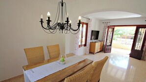 A dining area with a wooden table, wicker chairs, a chandelier, and a view through a glass door to the outside. - Galicia - private pool villa in Benissa (Benissa)