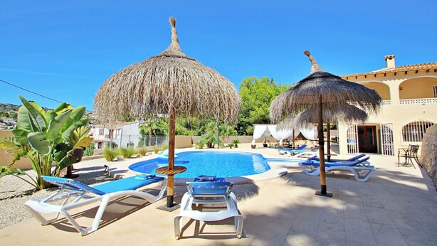A pool area with lounge chairs and thatched umbrellas, surrounded by a building with a tiled roof. - Galicia - private pool villa in Benissa (Benissa)