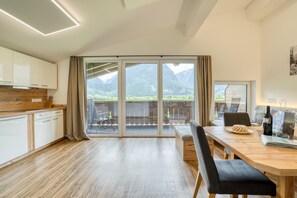 Eine moderne Küche mit Holzarbeitsplatte, ein Essbereich mit Tisch und Stühlen sowie große Schiebeglasfenster, die auf einen Balkon mit Bergblick führen.