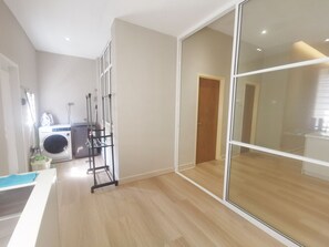 Una cocina moderna con lavadora integrada y un tendedero, suelo de madera y un amplio ventanal corredero que da a un pasillo.