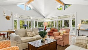 Un salon spacieux doté d’un haut plafond, de grandes fenêtres et de différents types de sièges, notamment un canapé, des fauteuils et un fauteuil à motifs.