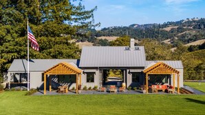 Une maison moderne dotée d’un patio couvert, d’un drapeau et, au loin, d’un vignoble.