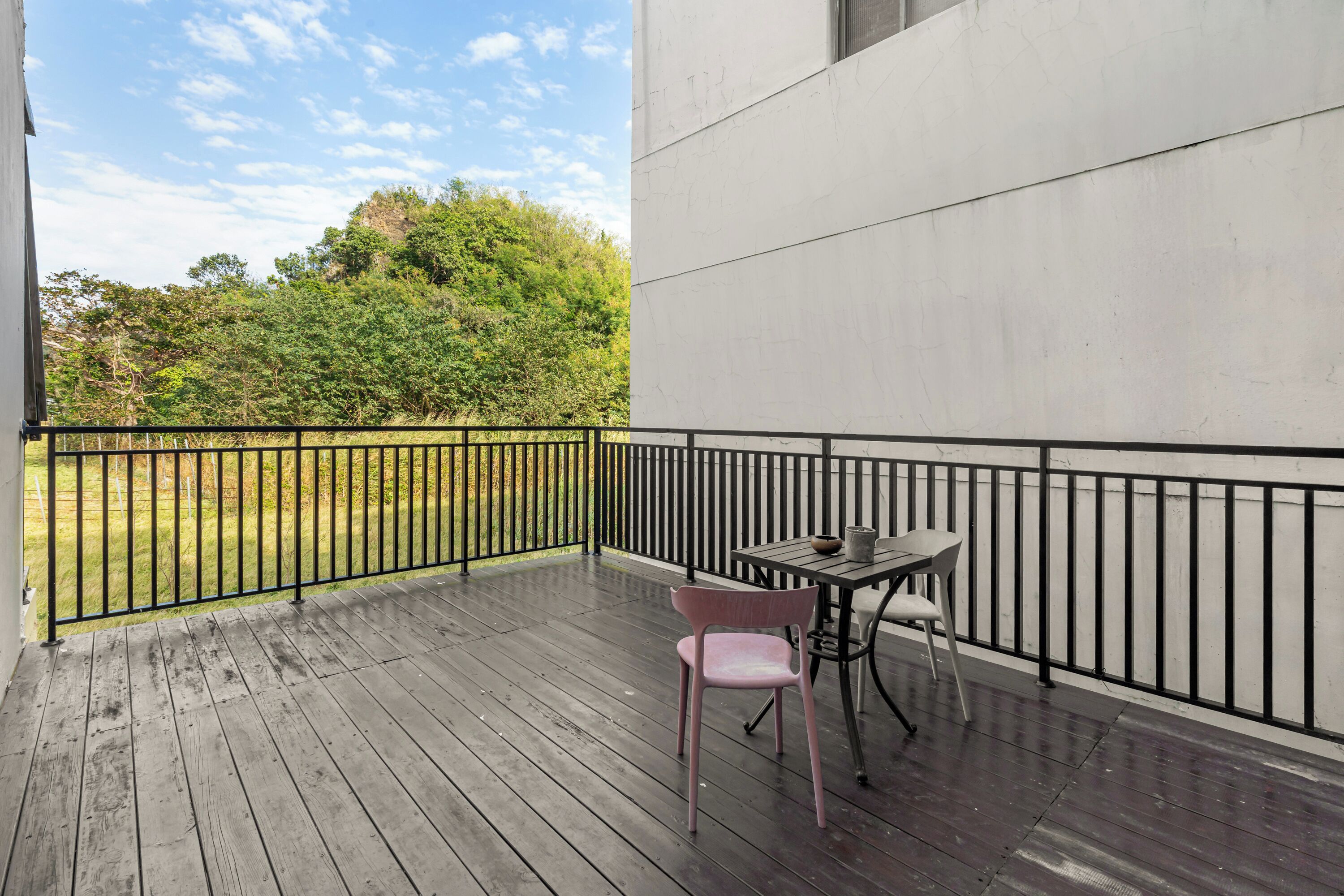 A wooden deck with a table and chairs, a black railing, and a view of trees and grass.