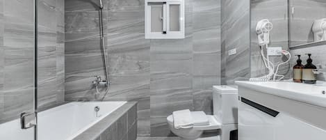 A modern bathroom with a bathtub, toilet, and a hairdryer on the counter.