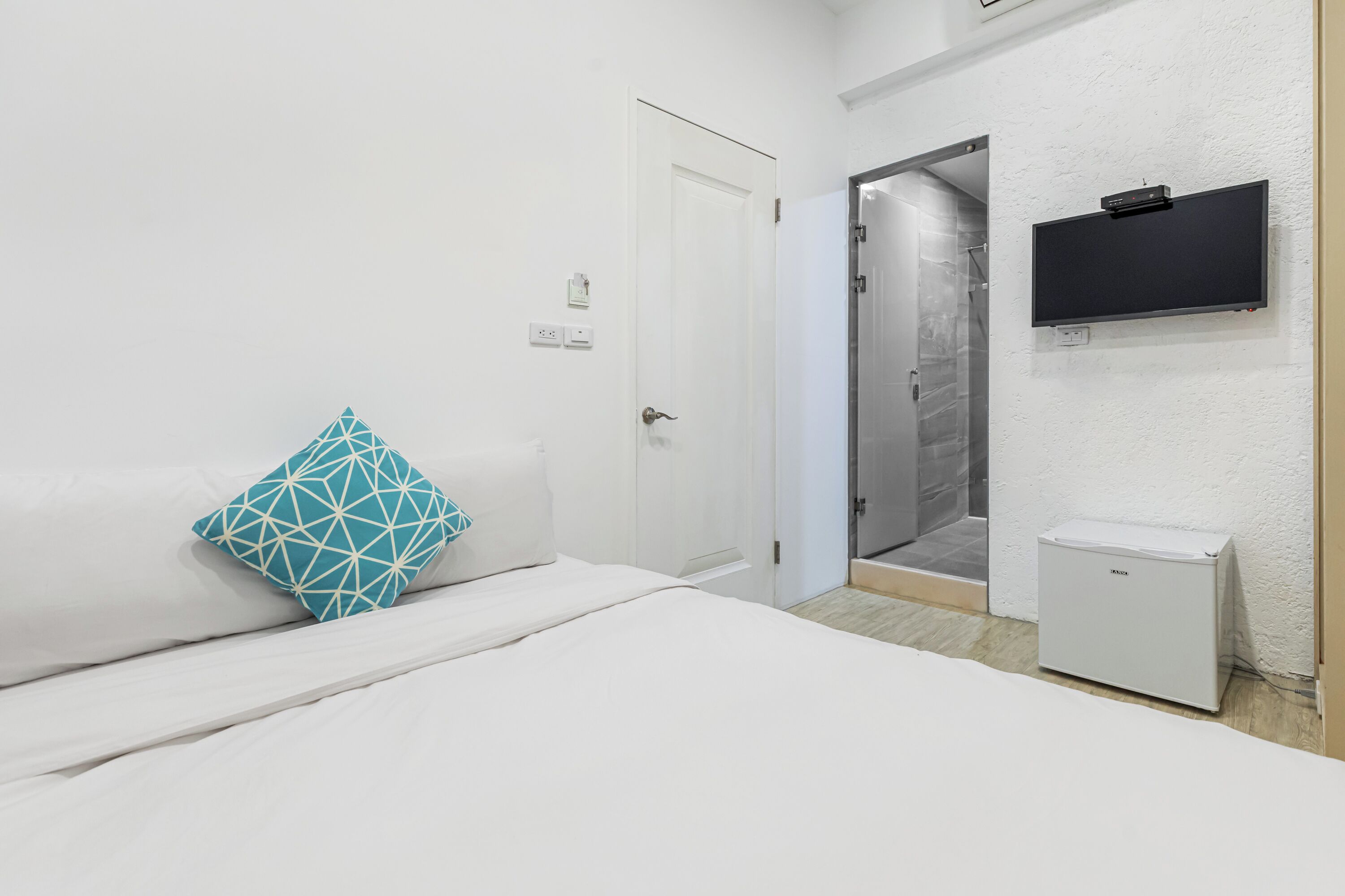 Un dormitorio con cama, una puerta blanca, zona de ducha y un pequeño electrodoméstico blanco.
