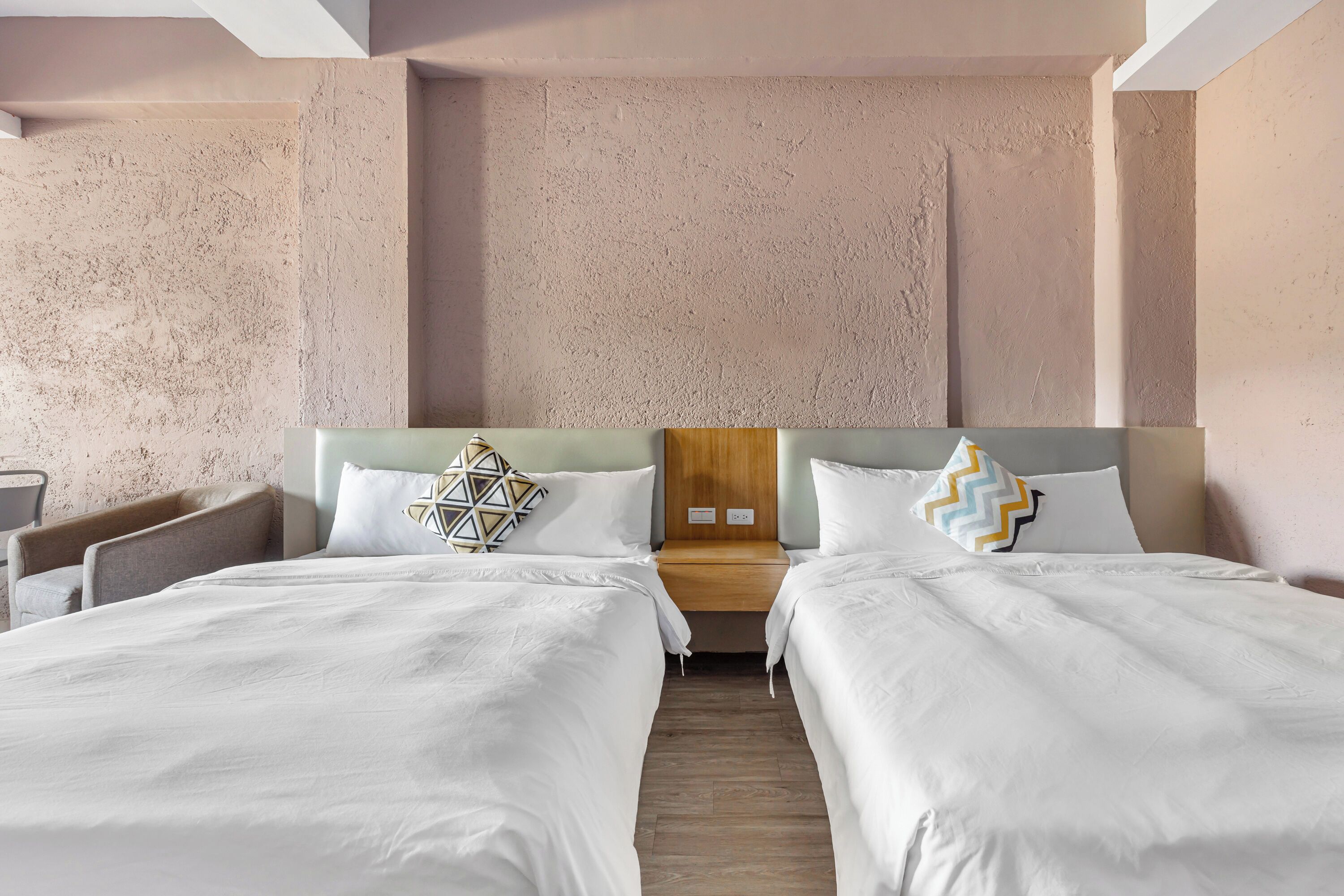 A hotel room with two beds, a wooden headboard, and a textured wall.