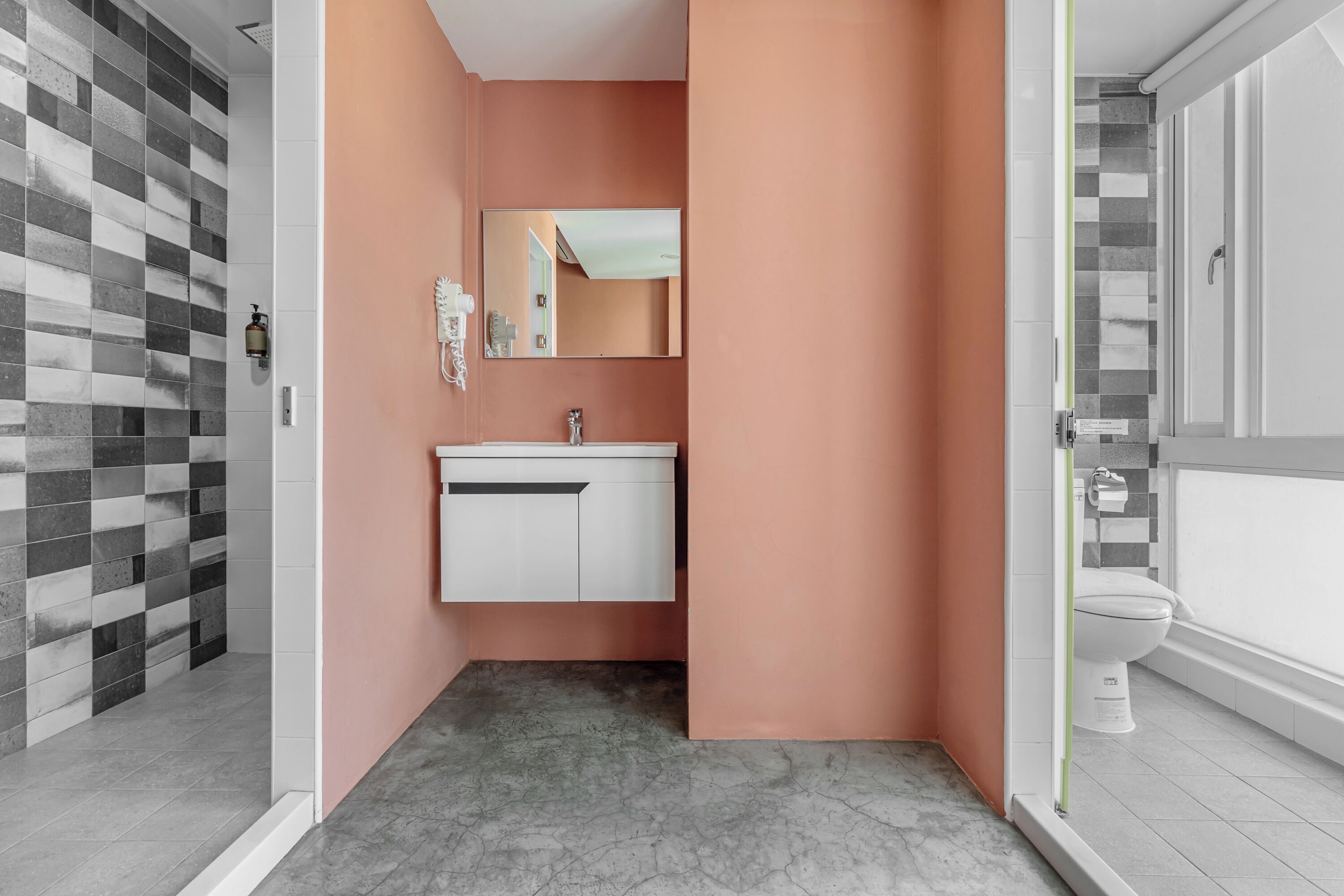 Une salle de bain avec un meuble-lavabo blanc, un miroir et un espace douche dont le mur est recouvert de carreaux à motifs.