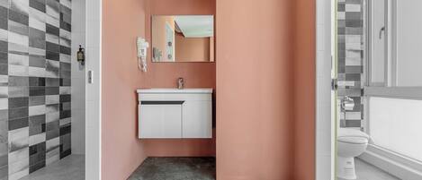 Une salle de bain avec un meuble-lavabo blanc, un miroir et un espace douche dont le mur est recouvert de carreaux à motifs.