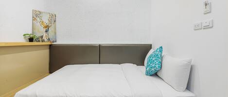 A neatly made bed with white bedding, a teal pillow, and a painting of a deer on the wall.