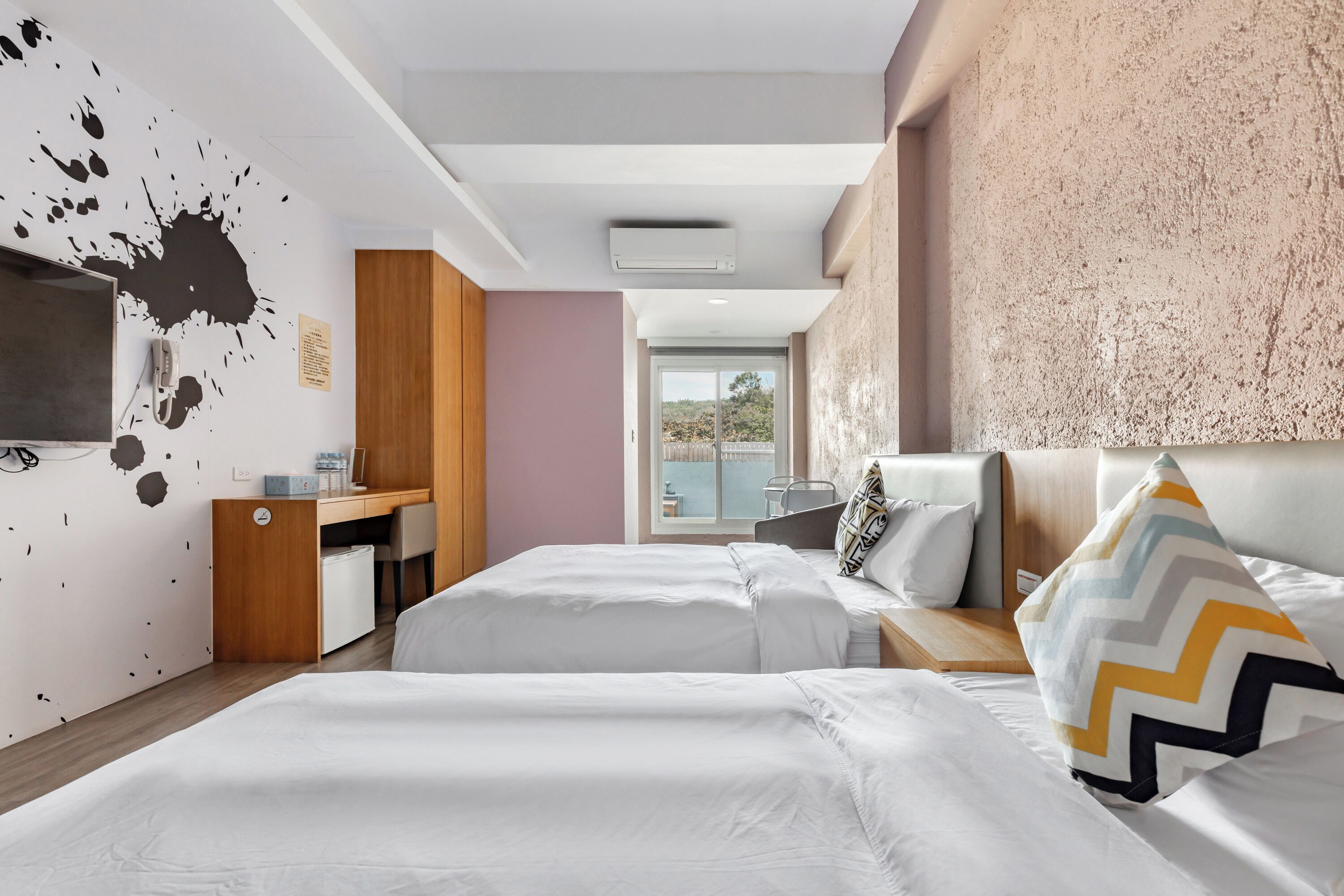 A hotel room with two beds, a desk, a chair, and a large window.