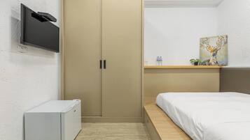 Un dormitorio con una cama, un armario, un televisor instalado en la pared y una estantería con un cuadro y una planta.