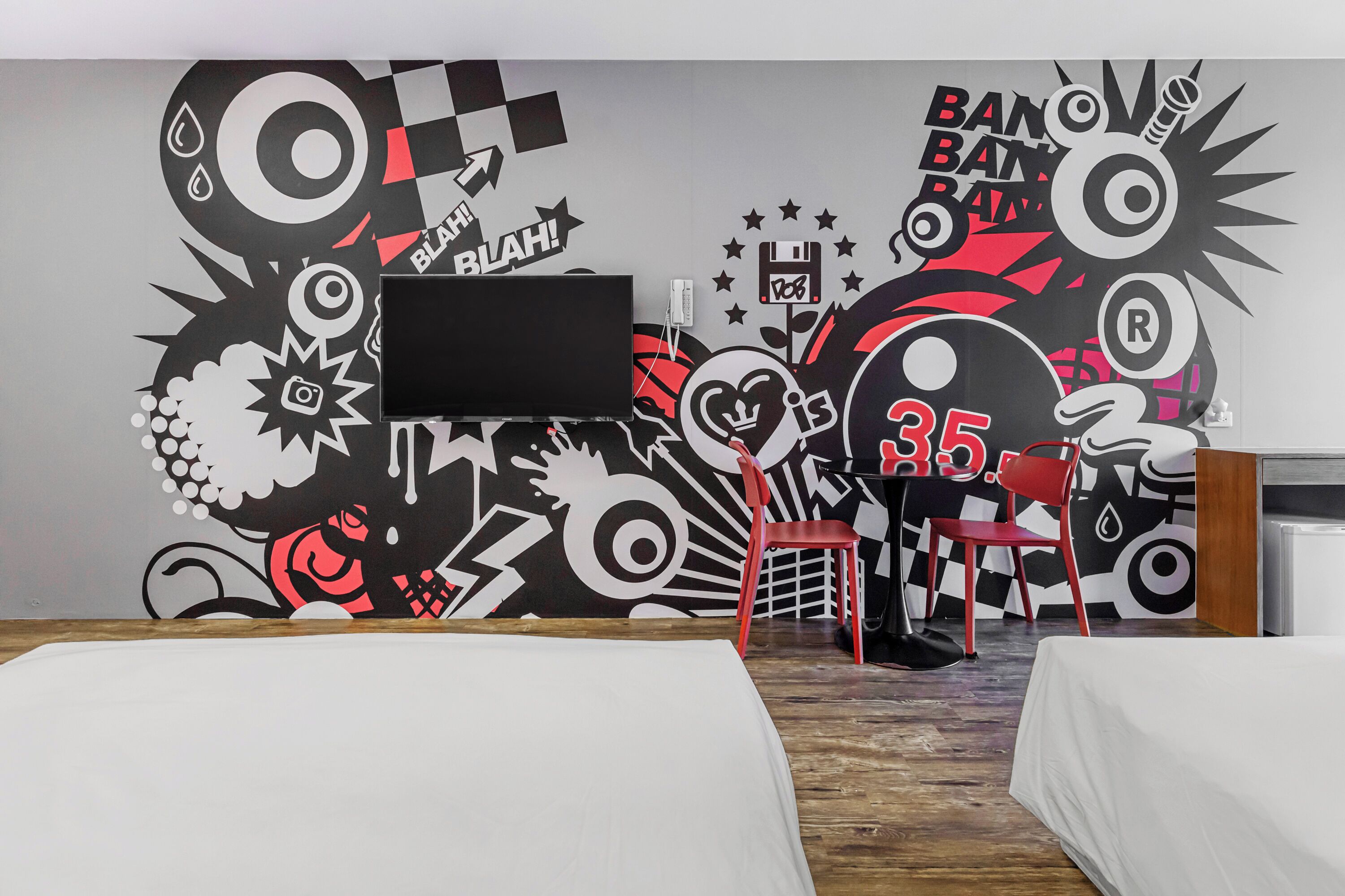 Une chambre d’hôtel avec une grande fresque murale, une télévision, deux lits simples, un bureau et une chaise.
