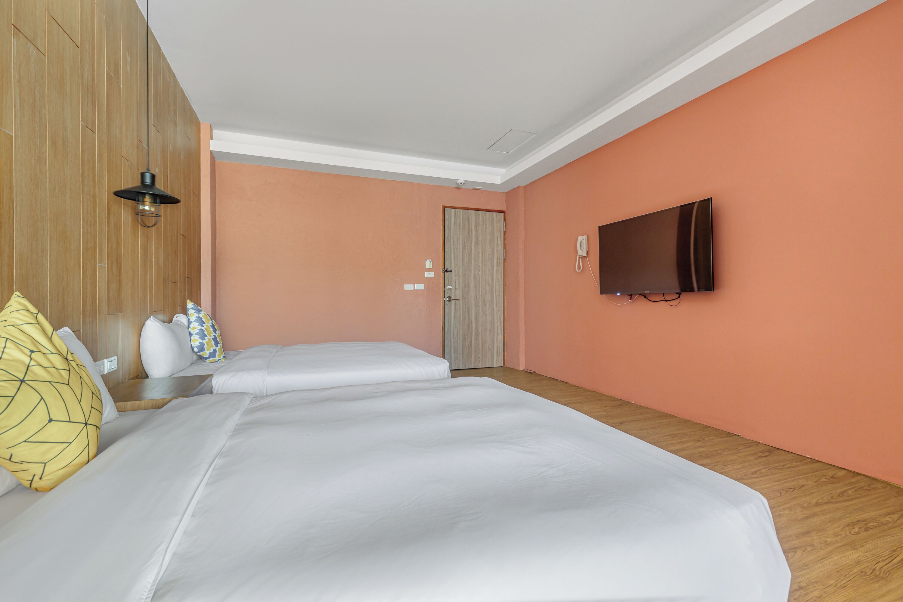 A hotel room with a large bed, a bedside table, a TV mounted on the wall, and a wooden door.