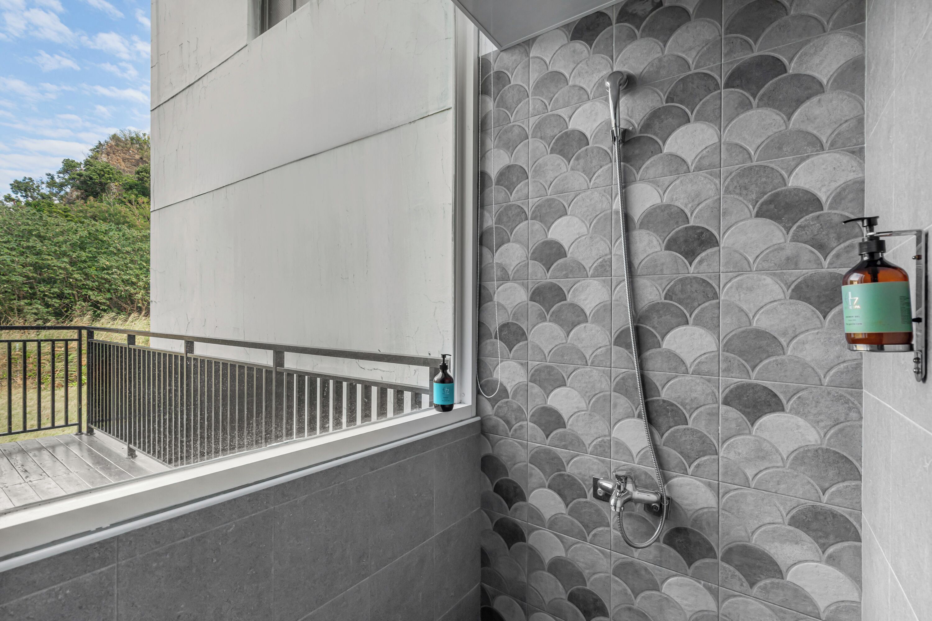 A bathroom with a tiled wall, a shower, and a bottle of soap on the wall.