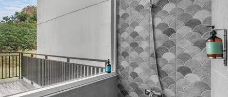 Un baño con pared de azulejos, ducha y una botella de jabón en la pared.