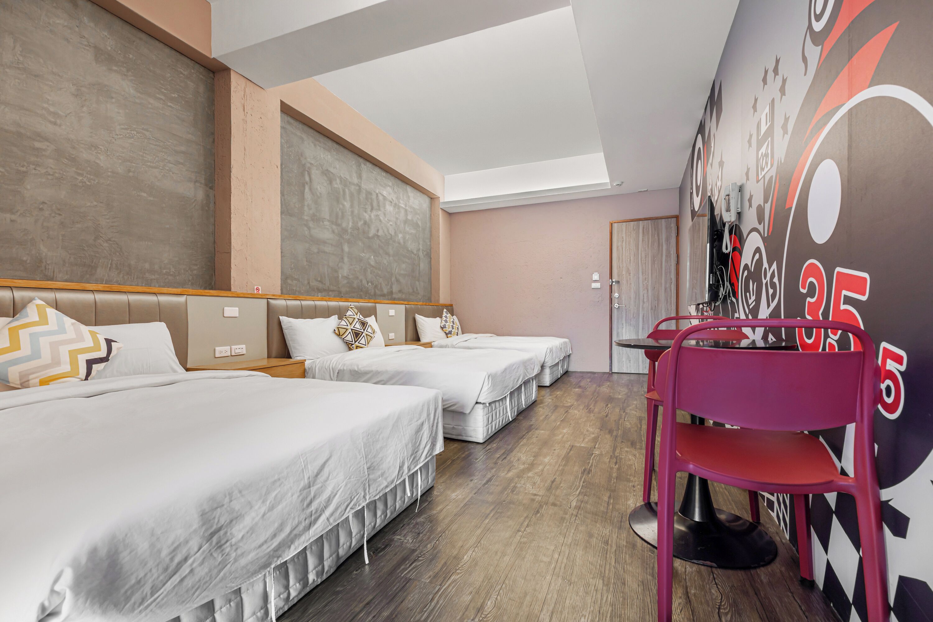 A hotel room with three beds, a desk, and a chair.