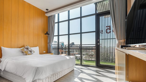 A modern hotel room with a large bed, wooden panel walls, a balcony with a view, and a kitchen area. - 35.5 inn (Hengchun)