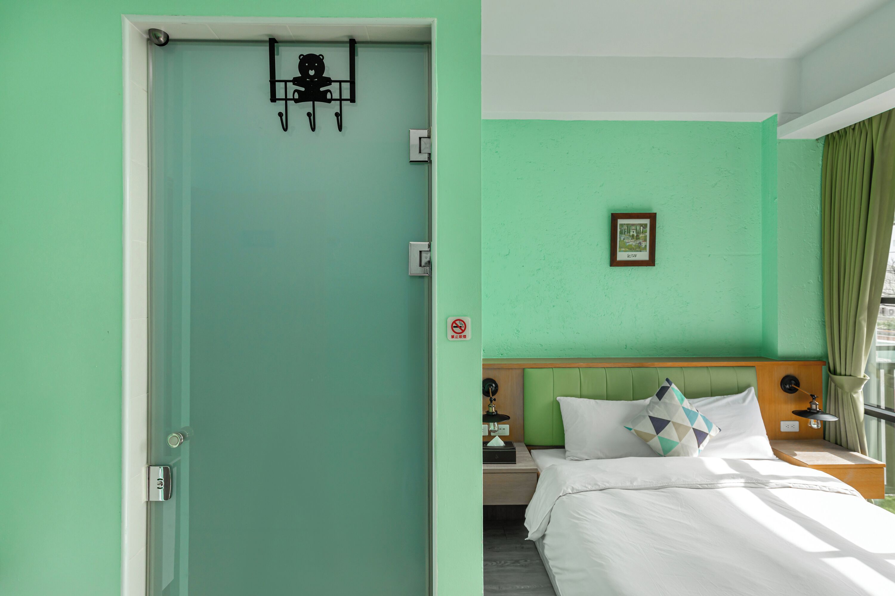 A hotel room with a green wall, a bed with white bedding, a nightstand, a lamp, and a framed picture on the wall.
