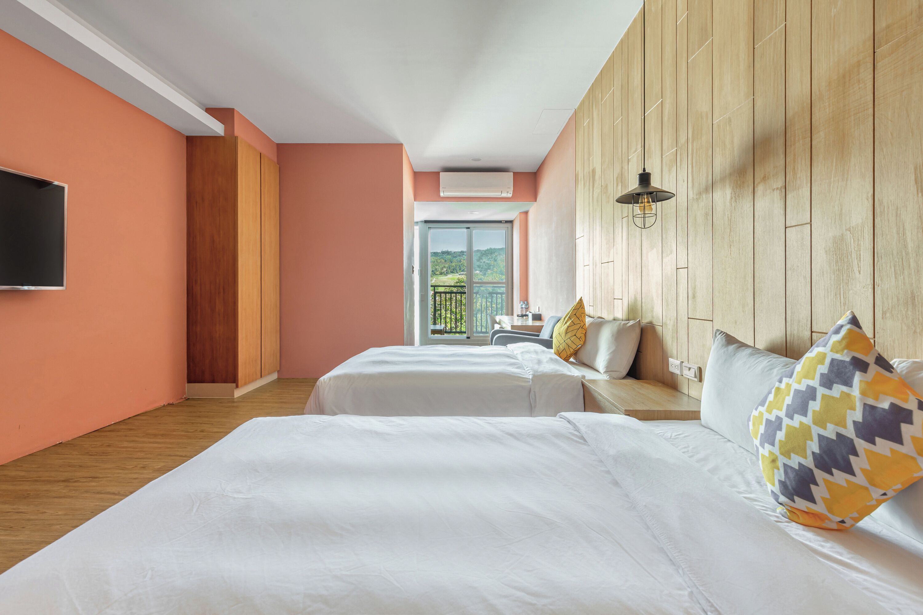 A hotel room with two beds, a TV, wooden paneling, and a balcony with a view.