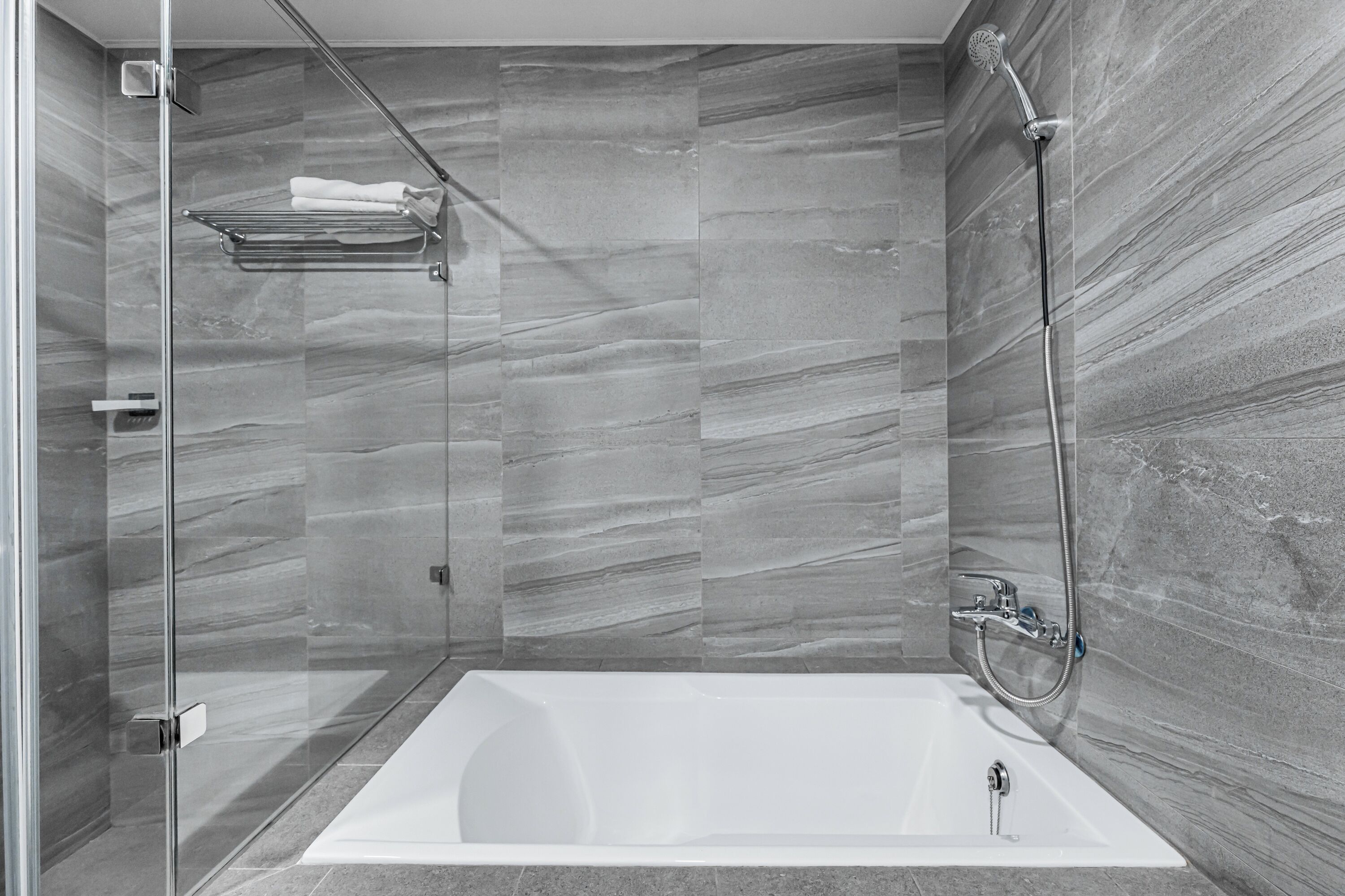A modern bathroom with a glass-enclosed shower, a white bathtub, and marble walls.