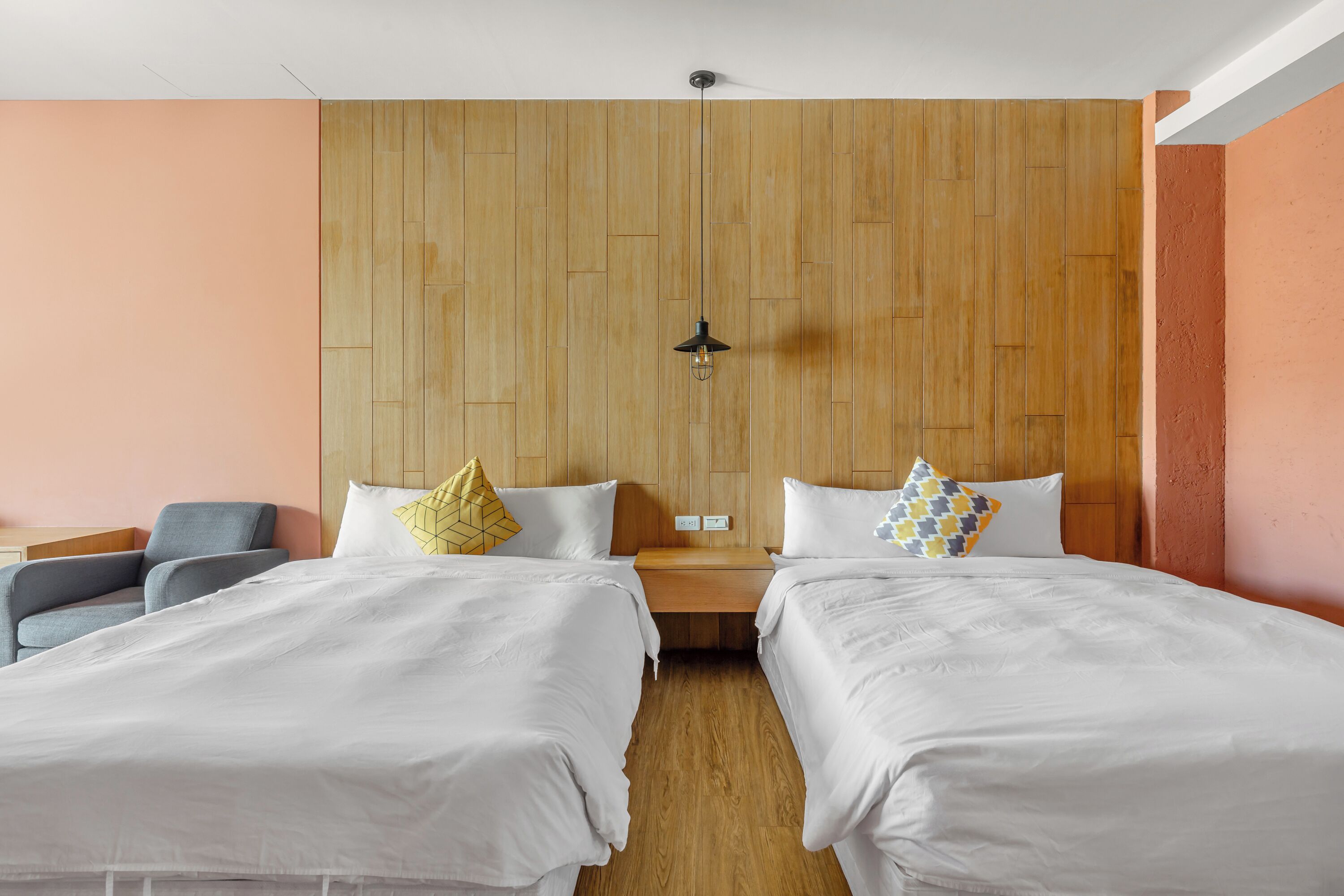A hotel room with two beds, a wooden headboard, a nightstand, and a chair.
