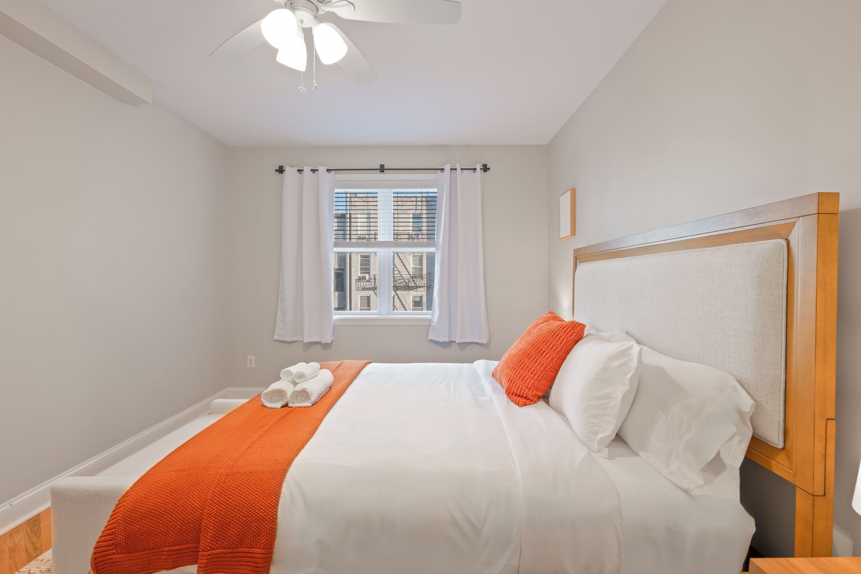Une chambre à coucher avec un lit, des rideaux blancs, une fenêtre avec des stores et un ventilateur de plafond.