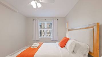 Une chambre à coucher avec un lit, des rideaux blancs, une fenêtre avec des stores et un ventilateur de plafond.