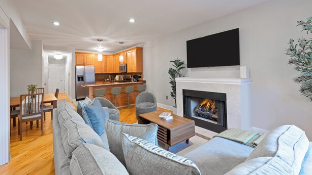 A modern living room with a fireplace, a dining area, and a kitchen.