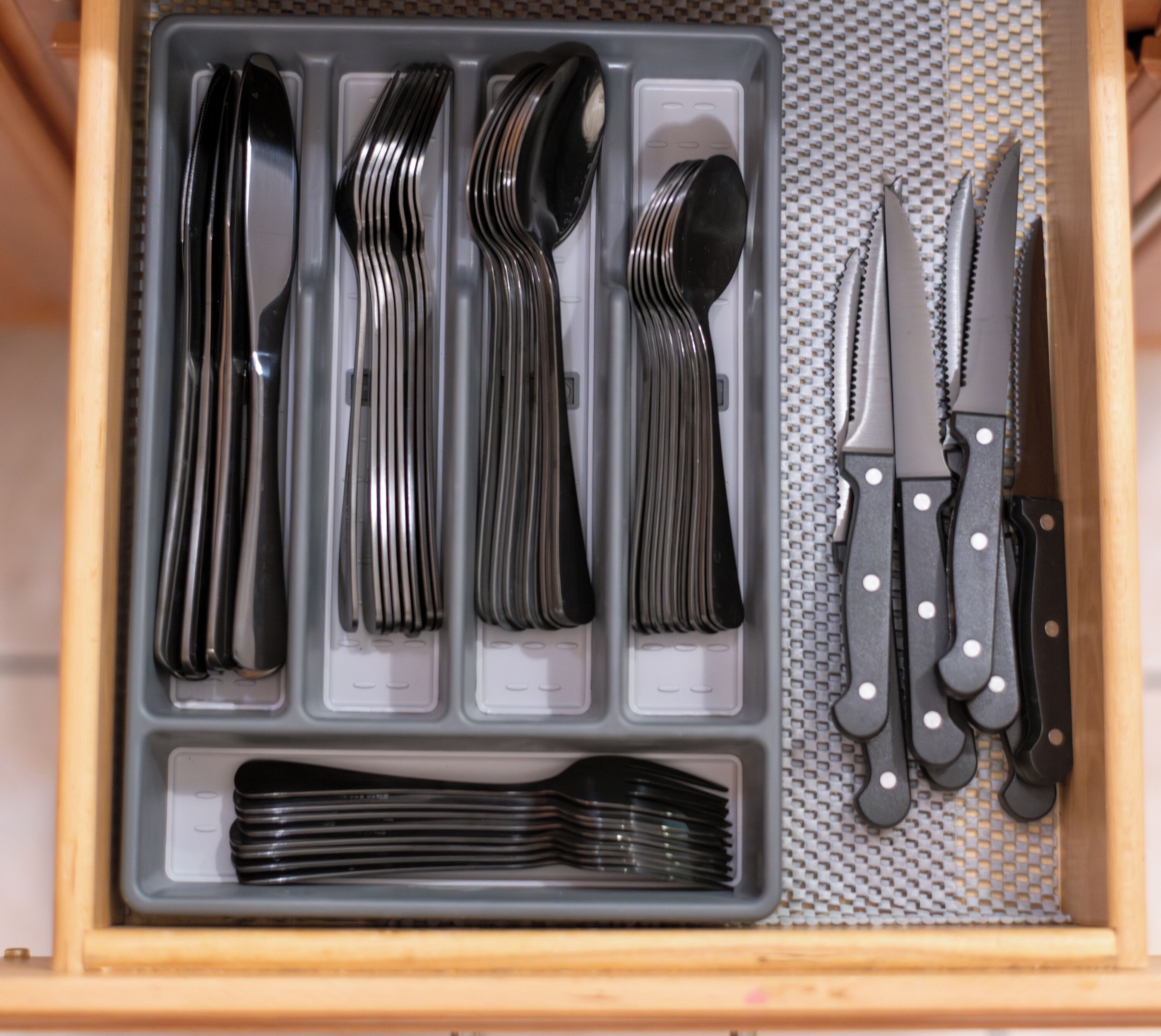 A drawer containing a set of utensils including forks, spoons, and knives, neatly organized in compartments.