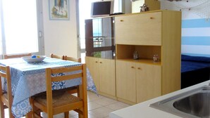A kitchen with a dining table, chairs, a wooden cabinet, a TV, and a window with curtains. - Holiday Home in Caorle Near Spiaggia Tartaruga (Caorle)