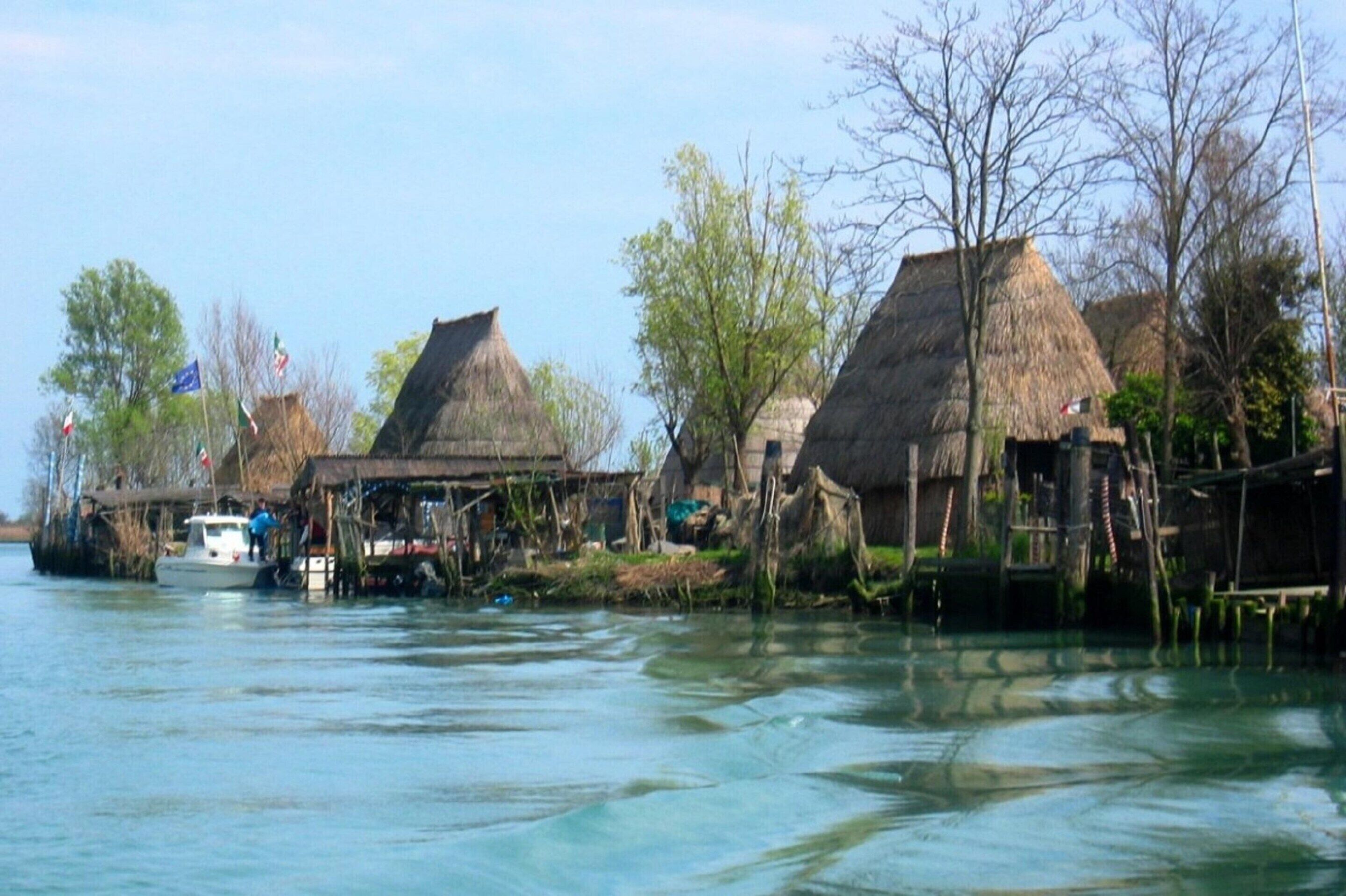 Ein Flussdorf mit reetgedeckten Häusern und einem Boot, das an der Ufer angelegt ist.