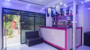 A reception area with a glass door leading outside, a seating area, and a bar counter with shelves of bottles. - Namaste Resort (Bhedetar)