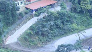 A hillside property with multiple buildings, including a main house with a red roof and a smaller structure with a similar roof. There is a staircase leading up to the buildings, surrounded by dense vegetation. - Namaste Resort (Bhedetar)