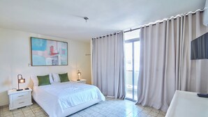 Una camera d'albergo con un letto, un comodino, una lampada, un quadro appeso e vista attraverso le tende.