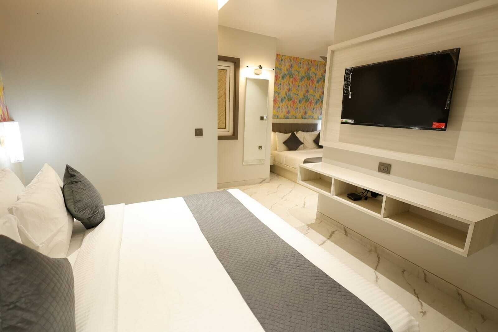 A modern hotel room with a large bed, a flat-screen TV mounted on the wall, and a small seating area with a colorful abstract wall art.