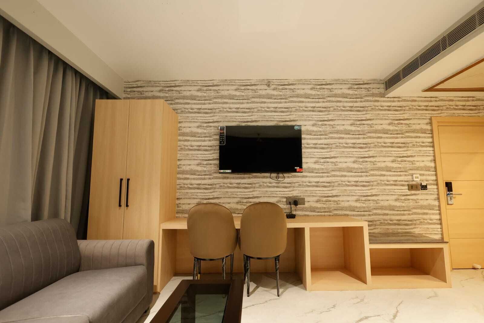 A modern hotel room with a sofa, a desk with two chairs, a television, and a wardrobe.