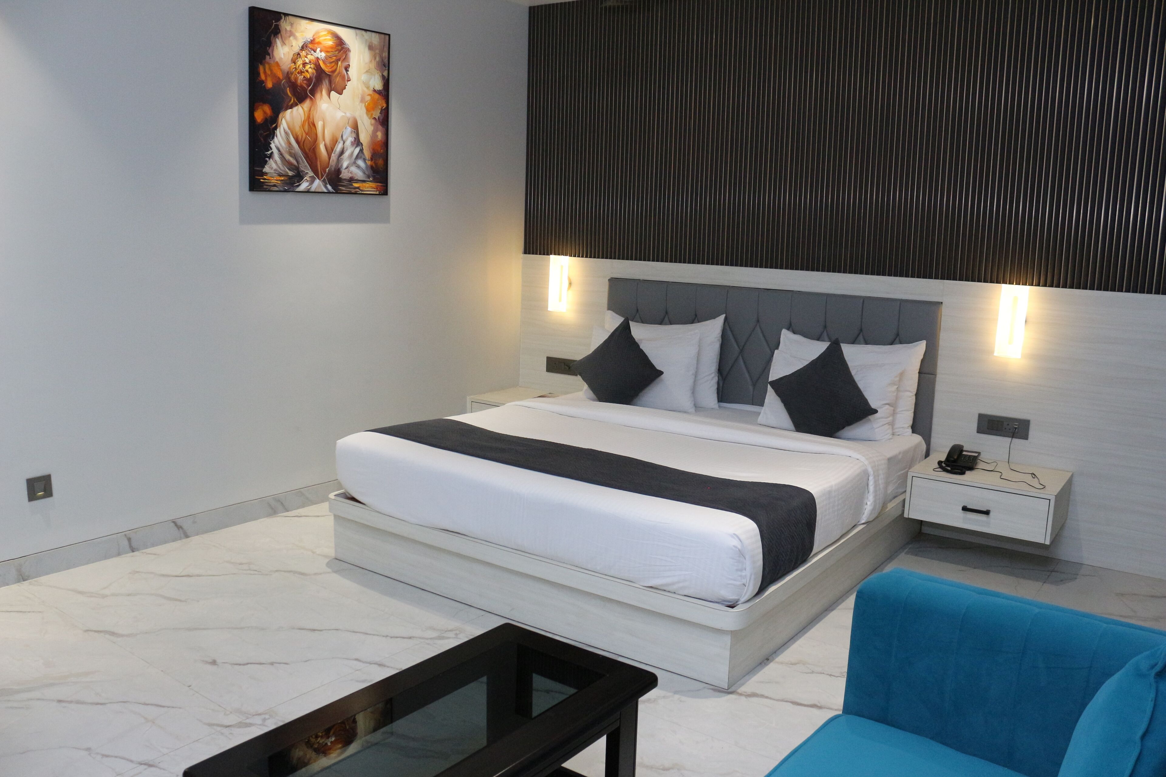 A modern bedroom with a large bed, bedside tables, a blue armchair, and a painting on the wall.