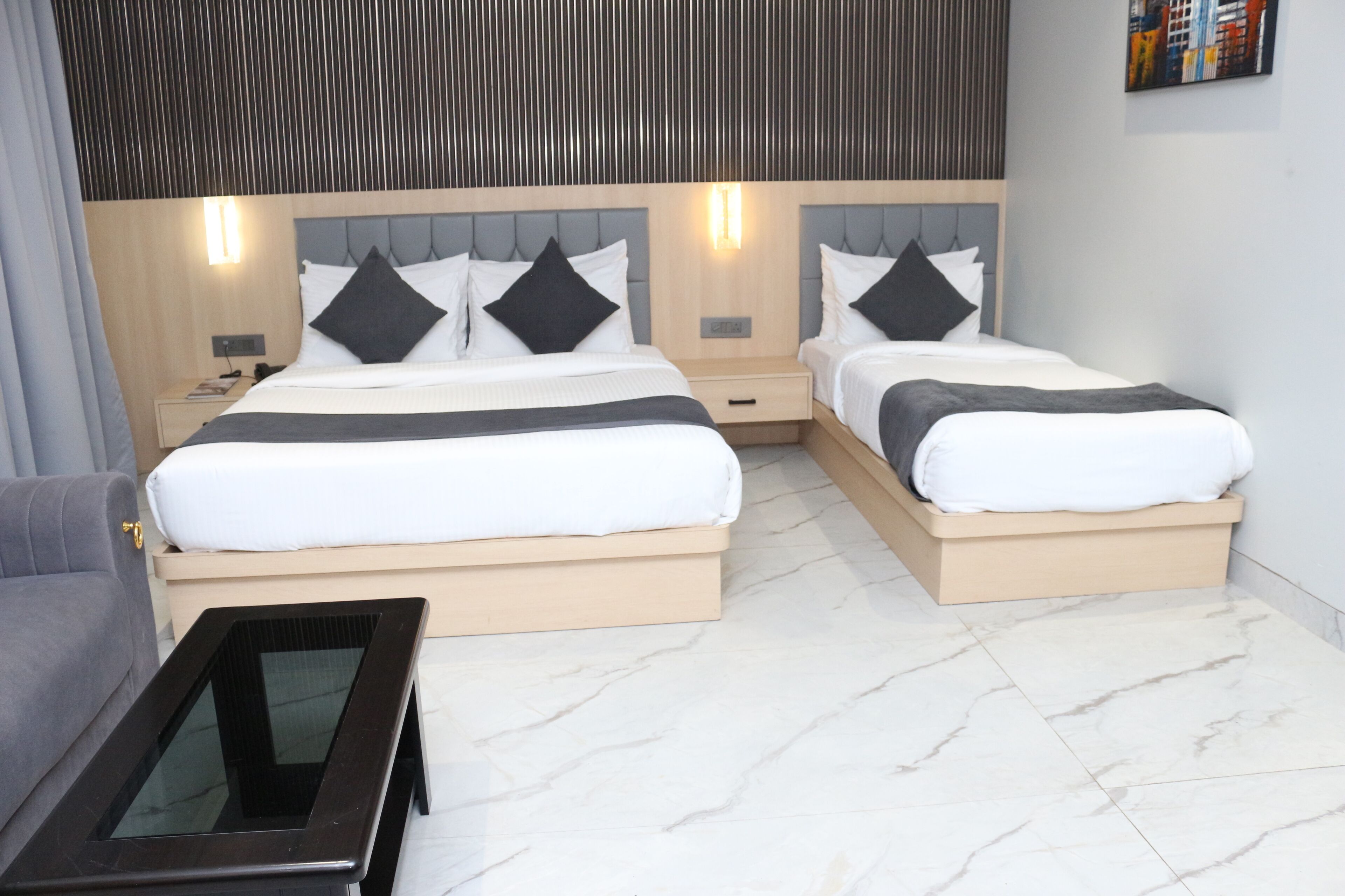 A modern hotel room with two beds, a small table, and a sofa.