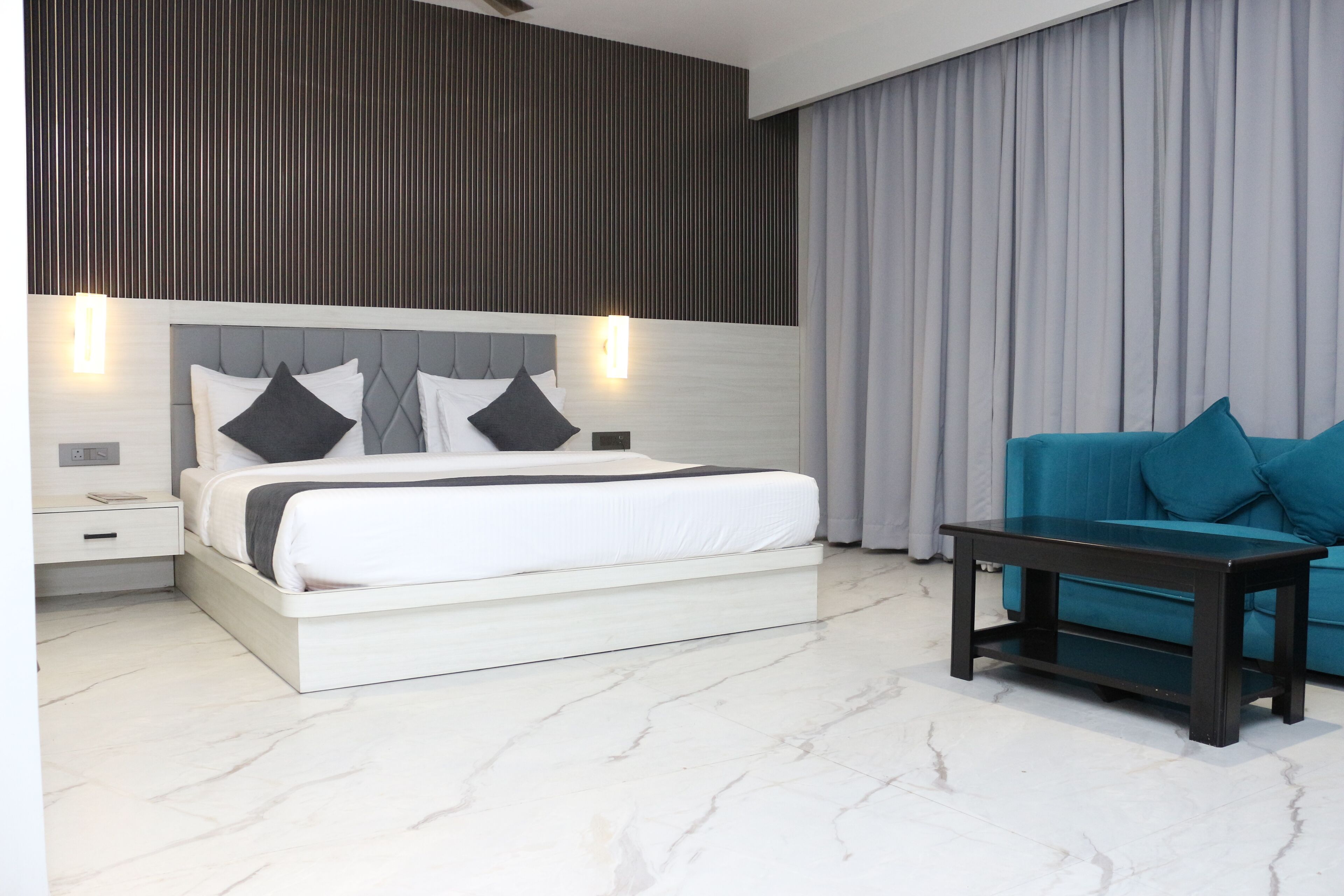 A modern bedroom with a large bed, bedside tables, a nightstand, a dark wooden bench, and a blue sofa.